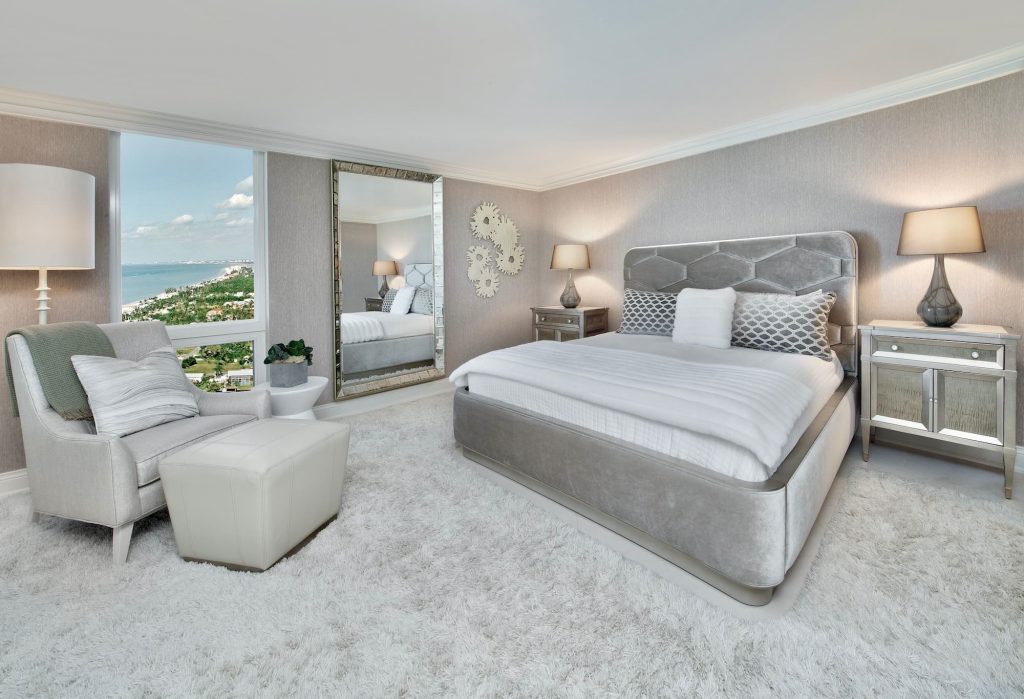 Rich contemporary master bedroom with shades of gray carpet, wall paper and fabric bedframe. Floor to ceiling mirror.